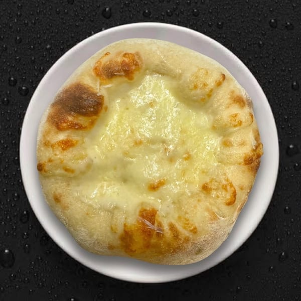 A round, cheesy khachapuri on a white plate, with a dark background.