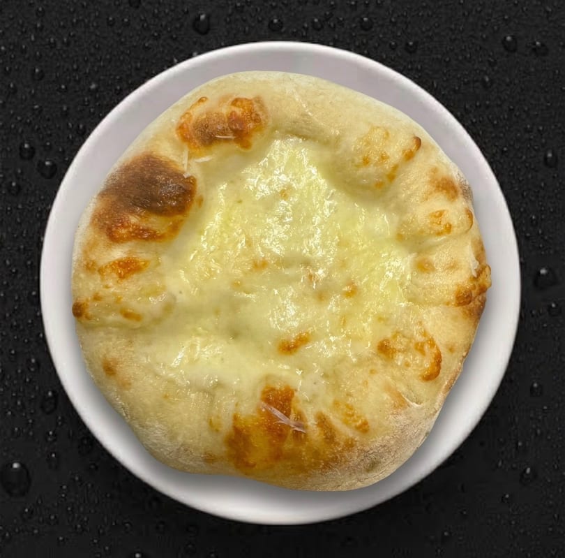 A round, cheesy khachapuri on a white plate, with a dark background.