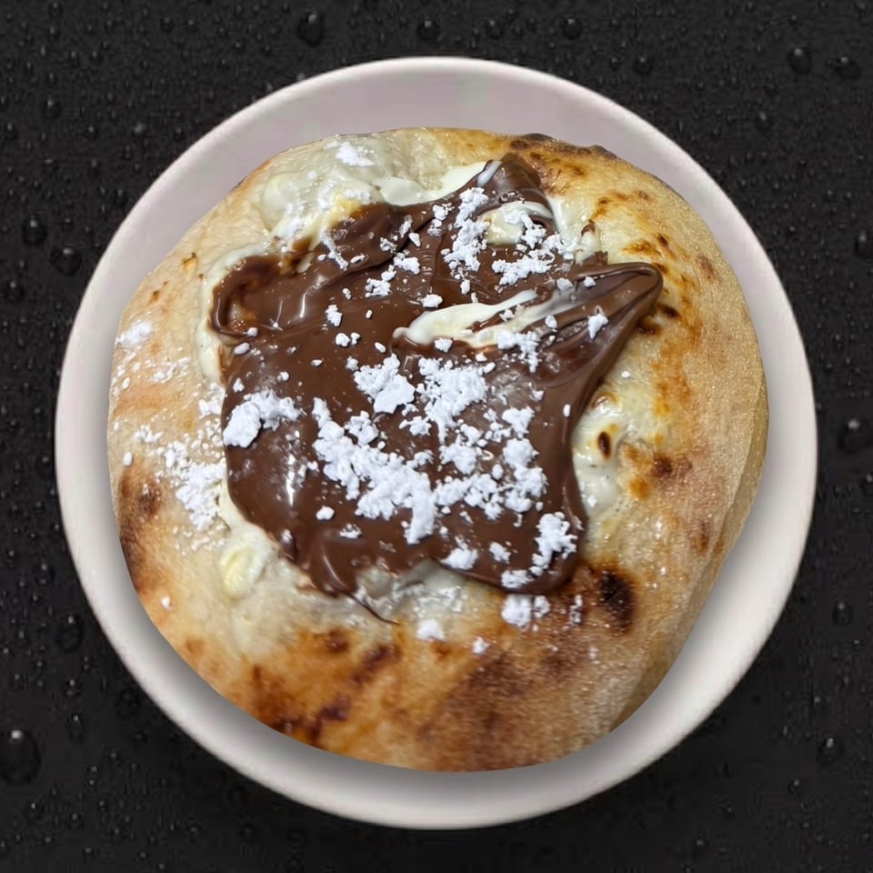 Dessert pizza with Nutella, white cream, and powdered sugar on a white plate.