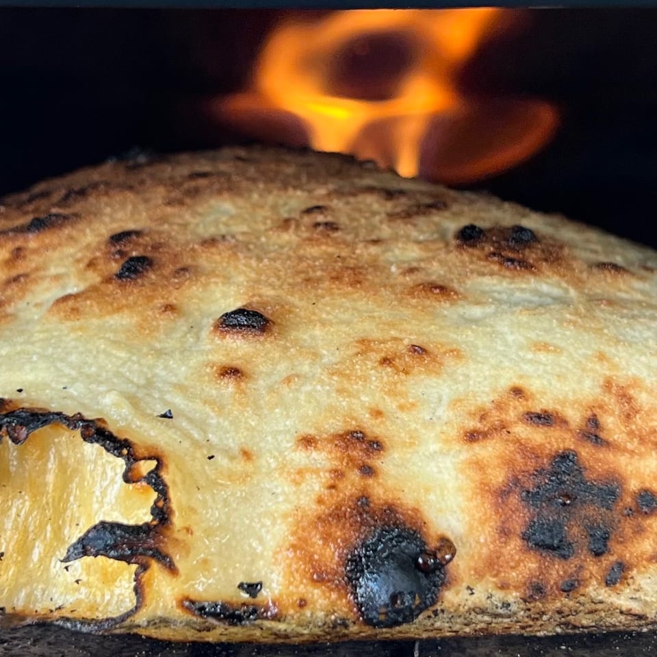 A calzone with a golden-brown crust and charred edges baking in a wood-fired oven.