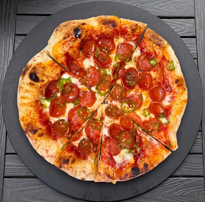 Pepperoni and jalapeño pizza, sliced and served on a black circular board on a dark wooden table.