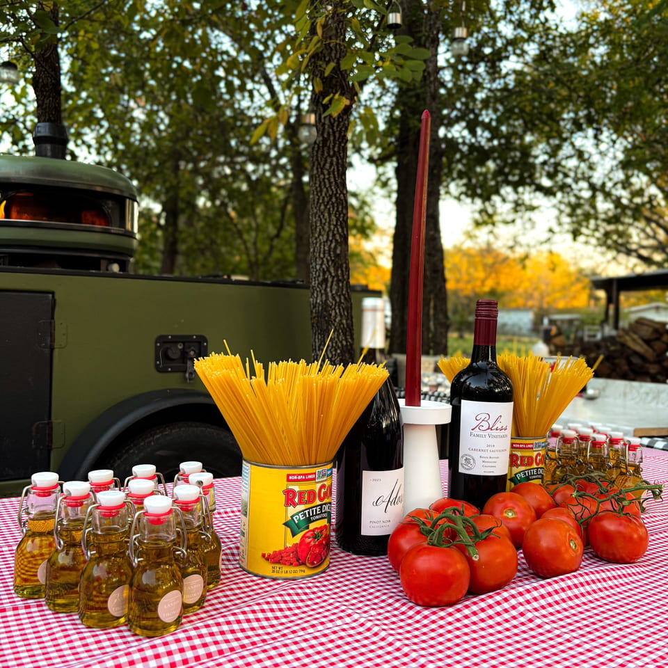 Italian ingredients like spaghetti, tomatoes, olive oil, and wine on a red and white checkered tablecloth.