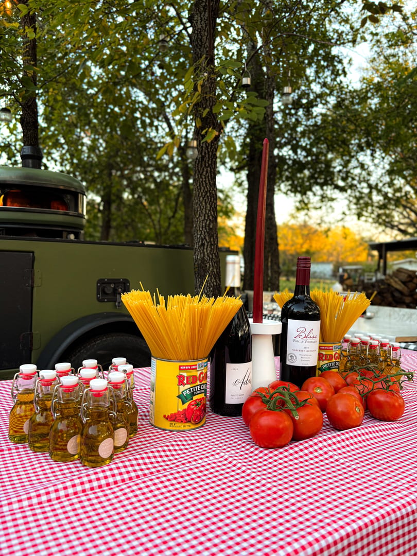 Italian ingredients like spaghetti, tomatoes, olive oil, and wine on a red and white checkered tablecloth.